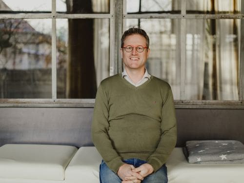 Simon Croonenbroeck sitzt auf einer Hypnoseliege, dem Betrachter zugewandt und blickt freundlich in die Kamera.